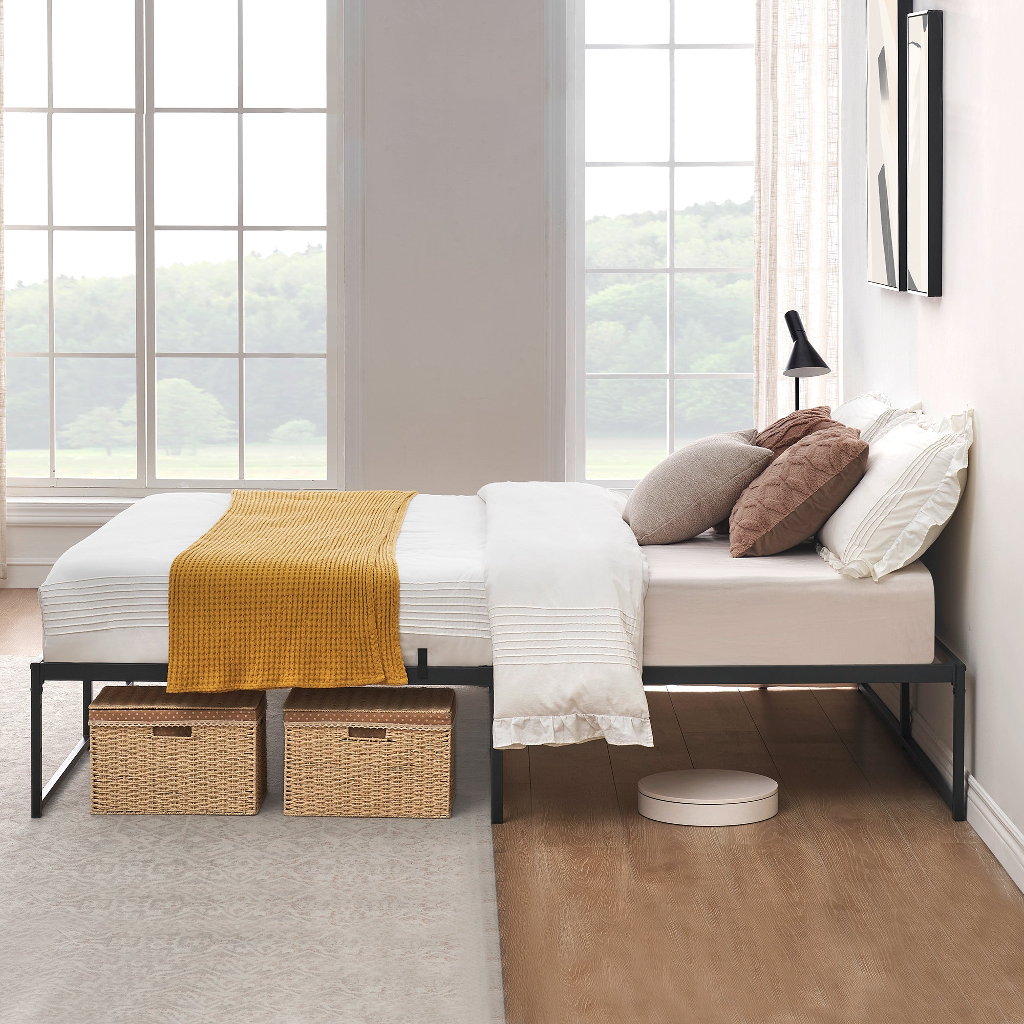 Black metal bed frame with a white mattress and two wicker storage baskets underneath.