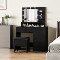 Black vanity table with large illuminated mirror, drawers, and shelves, placed in a room with a window and a bed.
