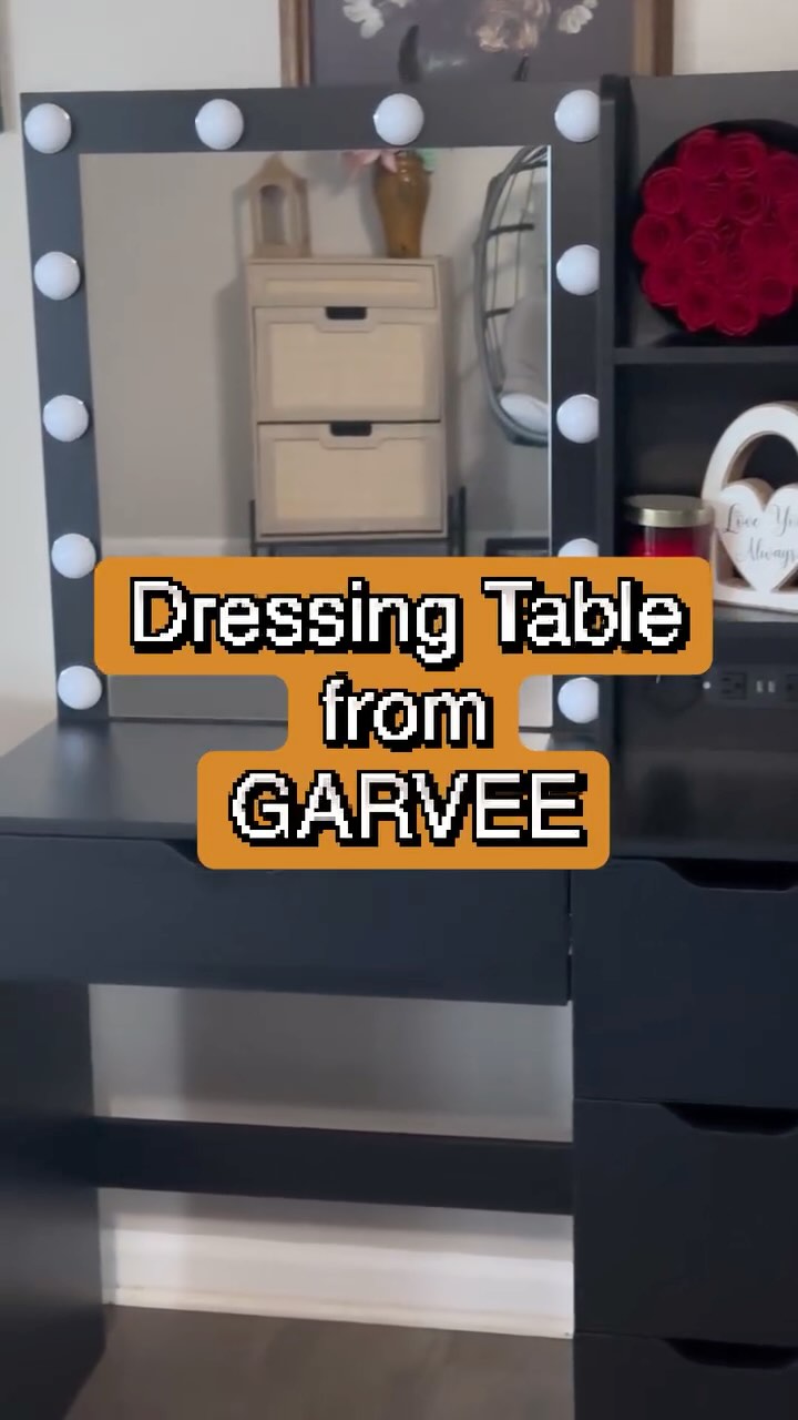 Black vanity table with illuminated mirror, multiple drawers, and shelves for makeup and beauty products, suitable for a bedroom or dressing room.