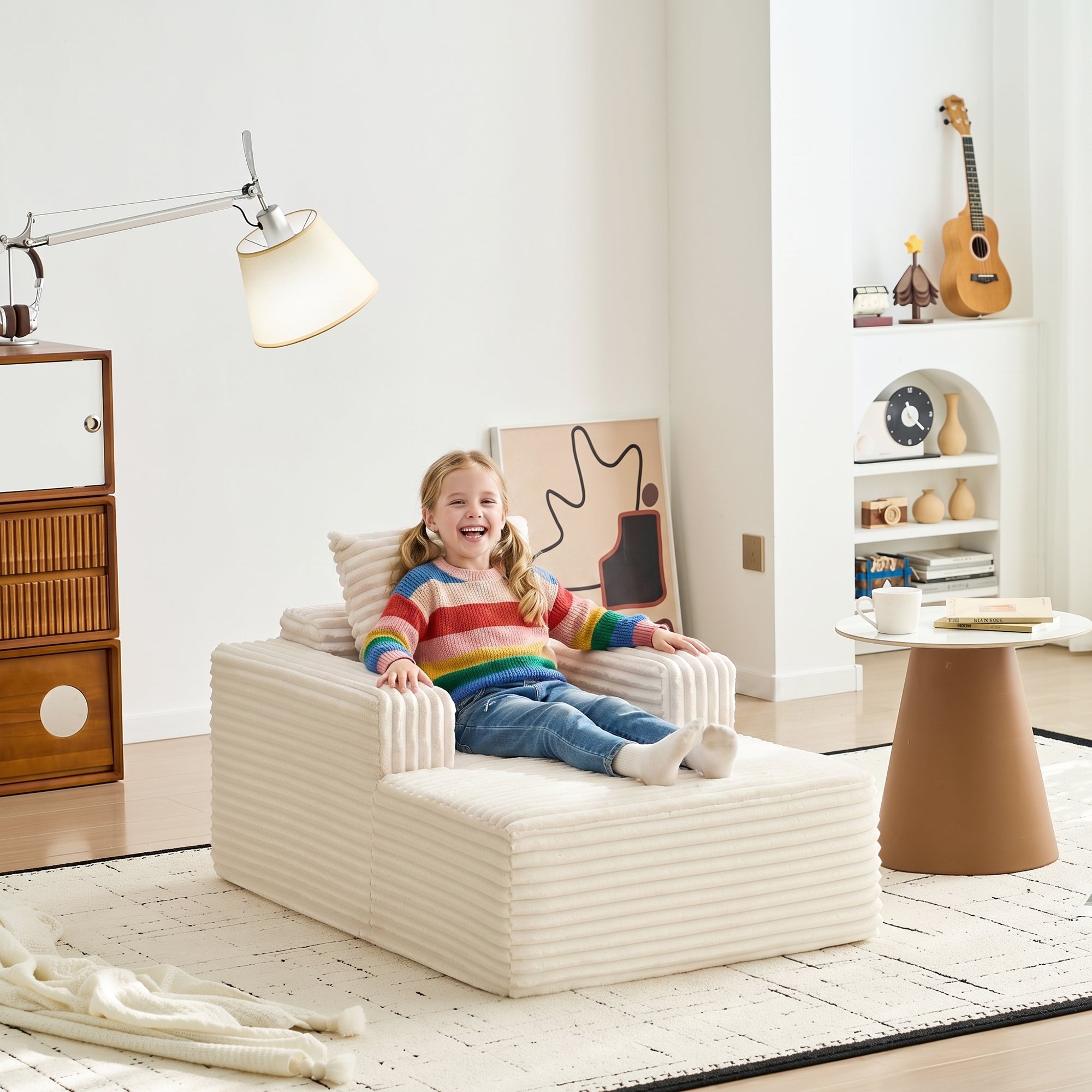 A young girl sitting on a cream corduroy chaise lounge chair.